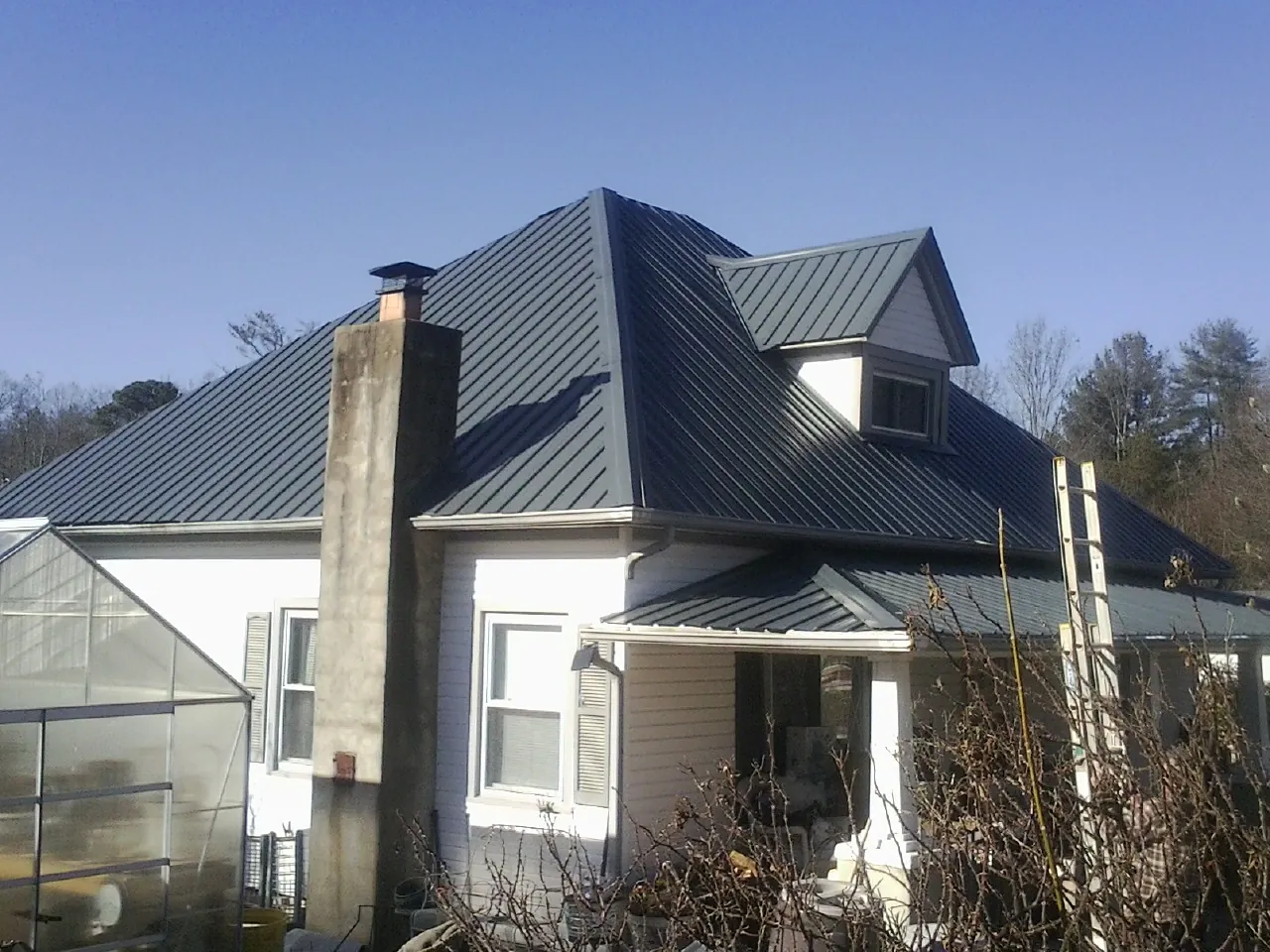 Dark blue standing seam metal roof on a white farmhouse with dormer — Slate & Tile Roof Repair by Roofing Brothers in Pine Hall
