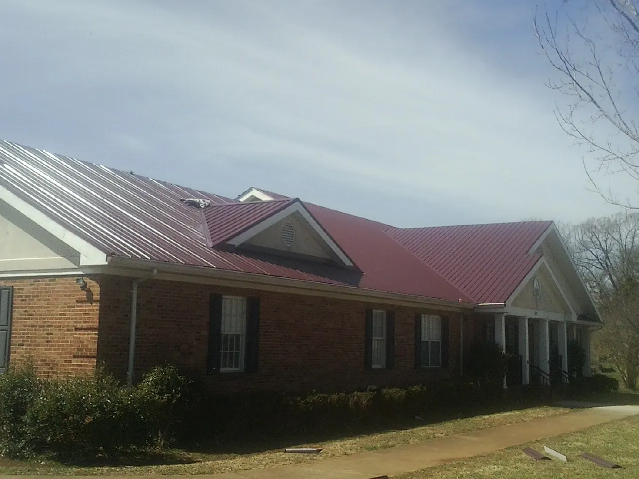 Red metal roof with gabled entries on a long brick building, from a Hail Damage Roof Repair job in Pine Hall