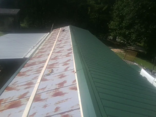 Old rusted panels beside newly installed green metal roofing — Wind Damage Roof Repair by Roofing Brothers in Pine Hall
