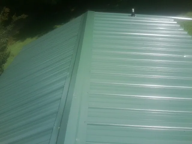 New green metal panels meeting at the ridge of a roof — Flat Roof Repair work by our crew in Pine Hall