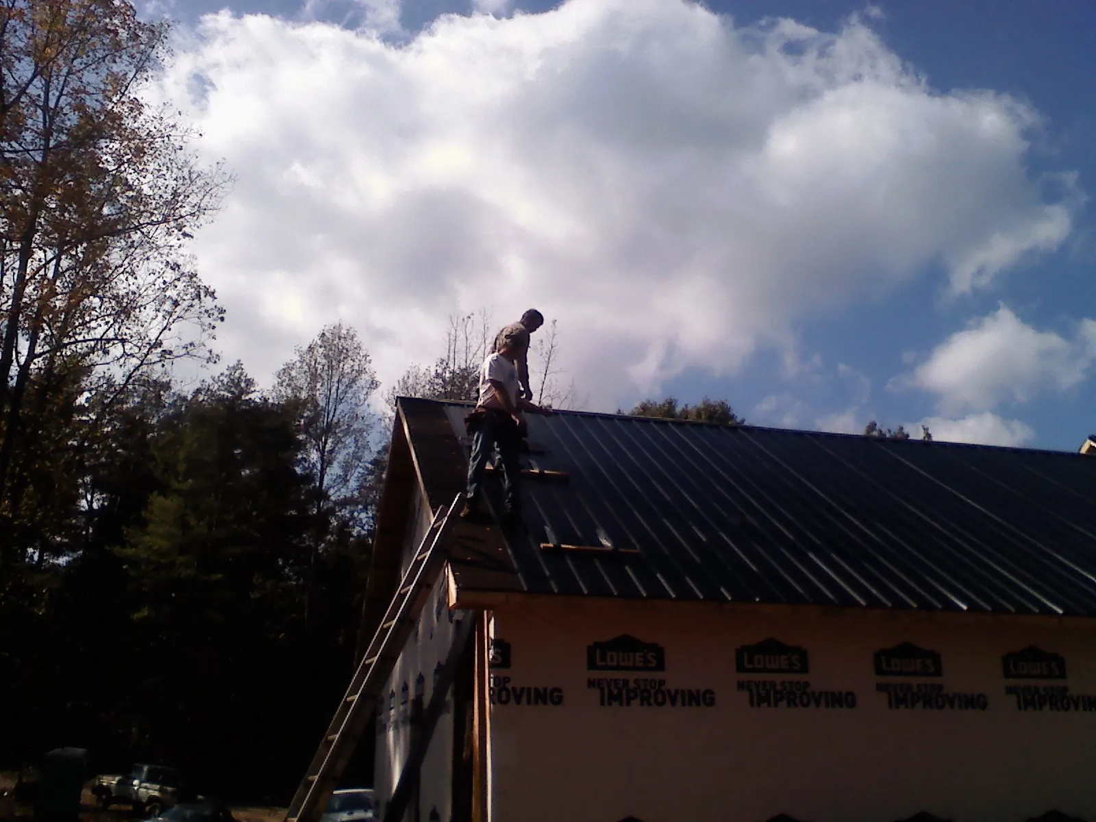 Roofer fastening dark metal panels high against a cloudy sky, from a Roof Inspection job in Pine Hall