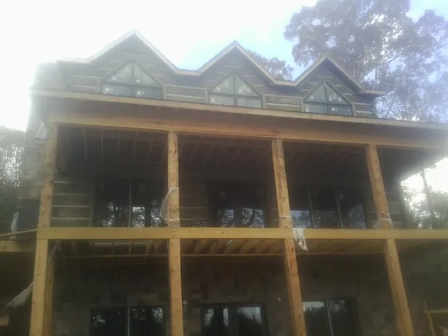 Dormers and porch framing on a large log home under construction — Roof Coating work by our crew in Pine Hall