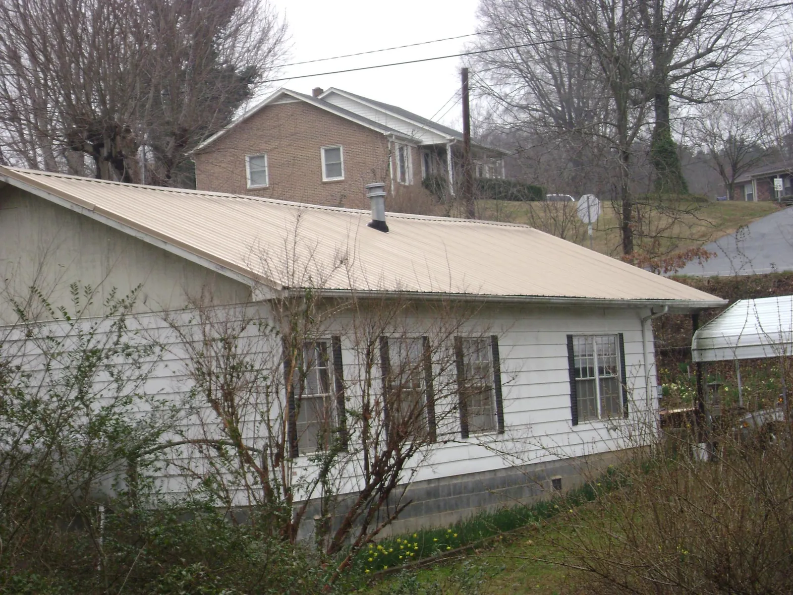 Tan metal roof on a white sided house set into a hillside — Commercial Roofing by Roofing Brothers in Pine Hall