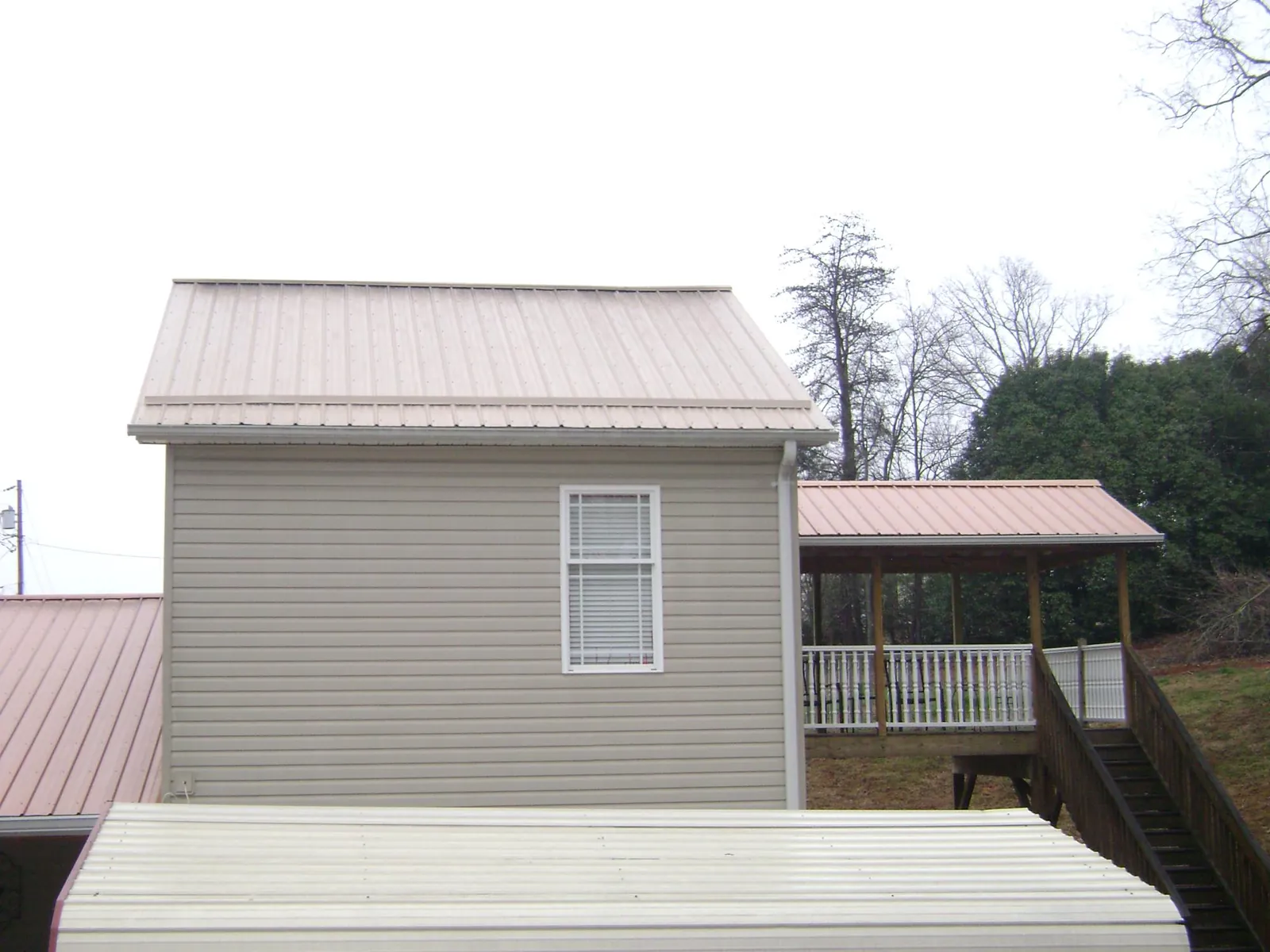 Tan metal roofs on a two story addition and attached porch, from a Roof Replacement job in Pine Hall